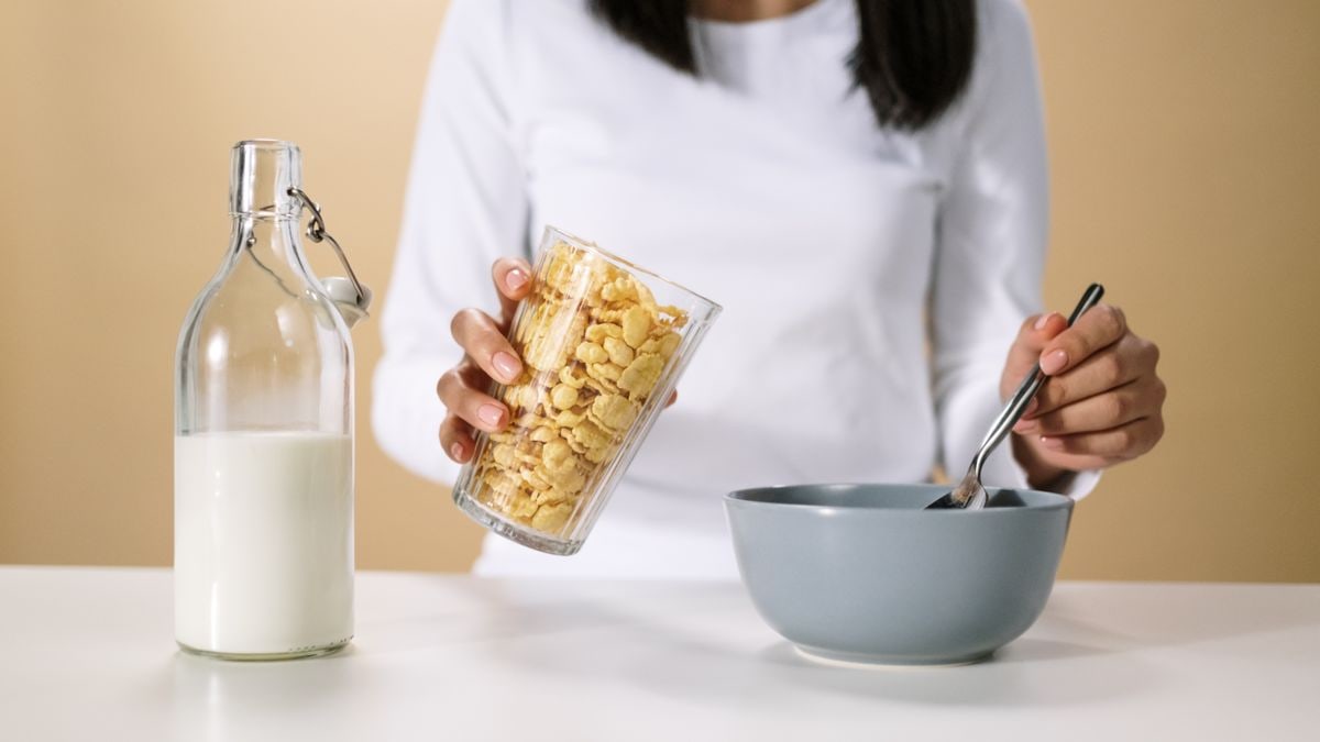 Person pouring cereal into a bowl with a bottle of milk nearby, ready for breakfast.
